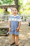 Baby boy standing outdoors wearing Smocked Hunting Jon Jon by Ruth and Ralph, blue gingham with smocked embroidery