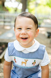 Close-up of baby boy smiling in Smocked Hunting Jon Jon by Ruth and Ralph, showing smocked deer and duck detail