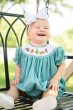 Close-up of baby girl smiling on porch swing wearing Smocked Camping Bubble by Ruth and Ralph