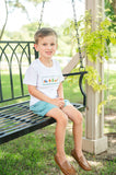 Boy sitting on swing outdoors wearing Camping Smocked Beau T-Shirt and Shorts Set, smiling