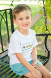 Boy wearing Camping Smocked Beau T-Shirt and Shorts Set, sitting on porch swing outdoors