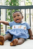 Baby wearing Smocked Hunting Bubble by Ruth and Ralph, blue gingham with smocked deer and duck embroidery, sitting outdoors