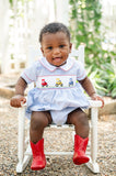 Baby boy in Ruth and Ralph Smocked Tractor Bubble, close-up seated in white chair outdoors