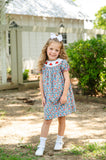 Girl standing outdoors wearing Smocked Floral Pumpkin Dress by Ruth and Ralph, blue floral print with white bow