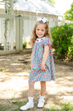 Girl standing on garden path wearing Smocked Floral Pumpkin Dress by Ruth and Ralph with white hair bow
