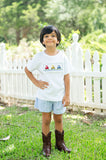 Boy wearing Smocked Tractor T-Shirt and Short Set by Ruth and Ralph, standing outdoors in front of a white picket fence