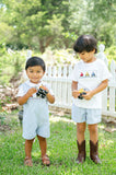 Two children wearing matching Smocked Tractor T-Shirt and Short Set by Ruth and Ralph outdoors