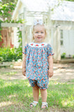 Baby girl standing outdoors wearing Smocked Floral Pumpkin Bloomer Set by Ruth and Ralph, blue floral print