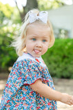 Close-up side profile of baby girl in Smocked Floral Pumpkin Bloomer Set by Ruth and Ralph, blue floral print with white bow