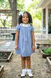Girl standing outdoors wearing Smocked Hunting Season Dress by Ruth and Ralph with white hair bow