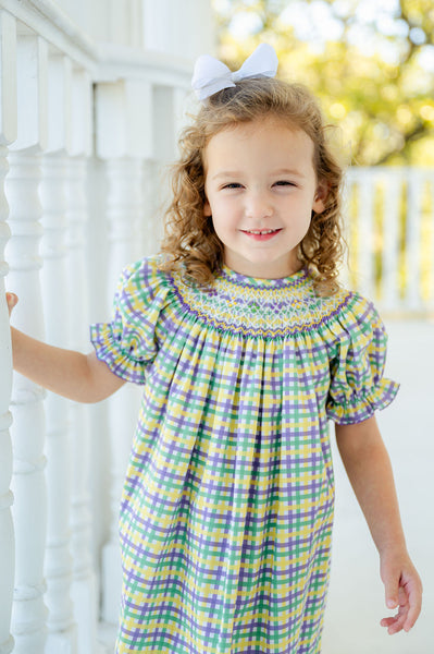 A girl in a smocked dress with green, yellow, and purple plaid looks festive and ready for Mardi Gras.