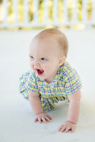 A baby in a vibrant plaid bubble with smocking, showcasing the spirit of Mardi Gras.