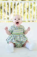 A baby in a beautifully crafted Mardi Gras bubble with green, yellow, and purple plaid accents.