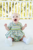 A baby in a beautifully crafted Mardi Gras bubble with green, yellow, and purple plaid accents.