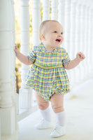 A baby in a green, yellow, and purple plaid smocked Mardi Gras bubble with intricate details.