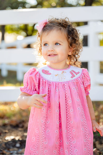 A little girl wearing the smocked Bandana and Boots Rodeo Helen Dress looks absolutely precious in its soft pink color and charming design.