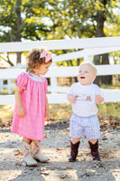 A little girl wearing the smocked Bandana and Boots Dress in pink looks adorable with its sweet western-inspired details.