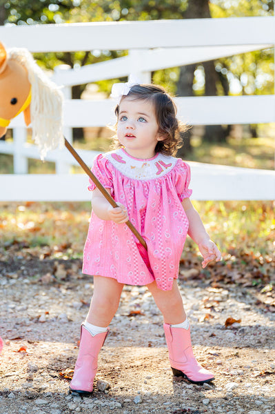 A little girl wearing the Smocked Pink Bandana and Boots Rodeo Annabelle Bloomer Set looks absolutely adorable in this playful, western-inspired outfit.