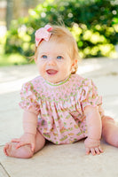 A baby girl wearing the Smocked Cowgirl Toile Birdie Bubble looks absolutely adorable in this western-inspired outfit.