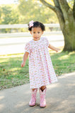 A girl wearing the Pink Cowgirl Toile Pima Catherine Dress looks charming in this soft, pink dress with a western-inspired toile print.