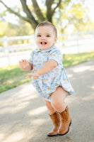 A toddler boy wearing the Blue Cowboy Toile Pima Alexander Bubble enjoys the softness and comfort of the pima cotton fabric, perfect for all-day wear.