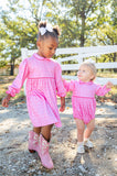 A little girl standing in the Pink Bandana Print Dress next to a baby wearing the matching Pink Bandana Print Bubble creates the sweetest moment, showcasing their coordinated western-inspired style.