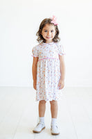 A toddler girl enjoys a day out in the Pima Puppies Dress, with its crisp white background and sweet Peter Pan collar.