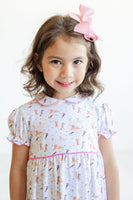 A little girl wearing the Pima Puppies Dress with pink piping looks adorable in the playful puppy print that covers the dress.