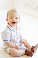 A toddler boy in the Pima Puppies Romper for boys smiles as the blue piping and classic collar add a stylish touch to his playful look.