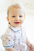 A little boy wearing the Pima Puppies Romper for boys with blue piping looks adorable, sporting playful puppies on a soft white background.