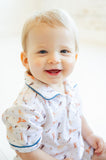 A little boy wearing the Pima Puppies Romper for boys with blue piping looks adorable, sporting playful puppies on a soft white background.