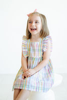 A little girl wearing the Colorful Plaid Dress with ruffle details looks absolutely charming in its vibrant, spring-ready plaid pattern.