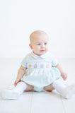 Dressed in the smocked mint green birthday cake bubble, a little boy is all smiles at his birthday party.