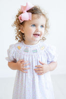 A little girl beams with joy in her smocked sprinkle birthday cake dress, perfect for her special day.