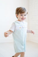 Wearing his smocked mint green jonjon, a little boy looks adorable, with festive birthday cake smocking for his milestone moment.