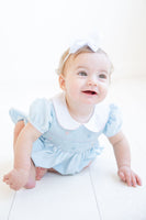 The Classic Blue Smocked Bubble is worn by a little girl, showcasing its delicate floral details.