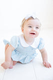 The Classic Blue Smocked Bubble is worn by a little girl, showcasing its delicate floral details.