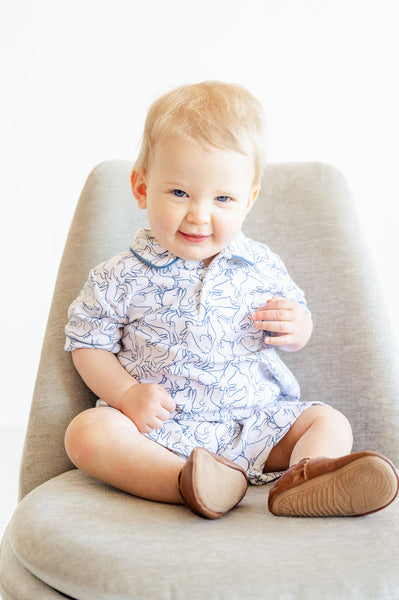 The Playful Bunnies Pima Harold Romper for baby and toddler boys features a fun bunny print with white bunnies outlined in blue, complemented by blue piping for a playful, fresh look.