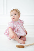 A baby in the Pink Golf Cart Smocked Bubble stands out with its cute pink argyle pattern, adding a touch of fun to her spring wardrobe.