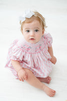 A little girl wearing the Pink Golf Cart Smocked Bubble is ready for any spring event, looking both adorable and stylish.