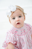 A baby girl wearing the Pink Golf Cart Smocked Bubble looks absolutely charming with its playful pink golf carts on the smocked bodice.