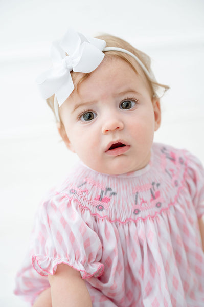 A baby girl wearing the Pink Golf Cart Smocked Bubble looks absolutely charming with its playful pink golf carts on the smocked bodice.