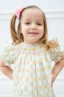 A little girl is wearing the Smocked Wildflower Dress, and its delicate light green and white checkered pattern makes her look absolutely charming.