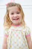 A little girl wearing the Pima Wildflower Dress with pink piping will shine in its cheerful light green and white checker pattern.