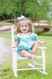 Baby girl sitting on white chair outdoors wearing Smocked Fall Gourds Bubble with white hair bow