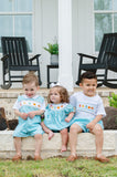 Three children sitting on steps wearing matching Smocked Fall Gourds outfits outdoors