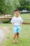 Boy wearing Smocked Fall Gourds T-Shirt and Shorts Set, standing outdoors near bridge and pond