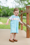 Toddler standing outdoors wearing Smocked Fall Gourds Jon Jon by Ruth and Ralph, light blue with smocked gourd embroidery