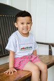 Boy sitting on wooden bench wearing Smocked Race Car T-Shirt and Shorts Set, red gingham shorts