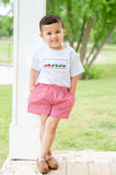 Boy standing outdoors wearing Smocked Race Car T-Shirt and Shorts Set with red gingham shorts